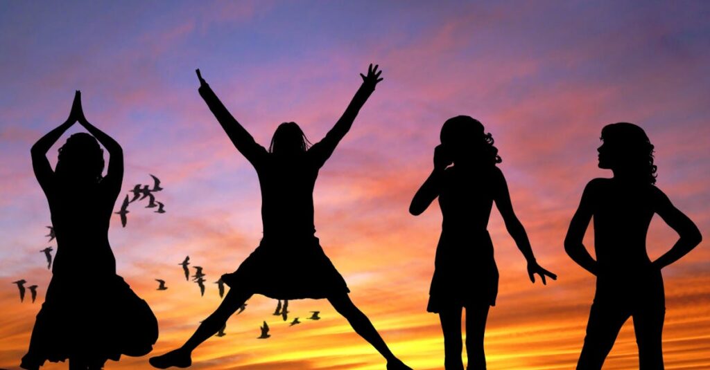 Silhouetted group of women joyfully jumping and posing against a vibrant sunset sky with birds flying.