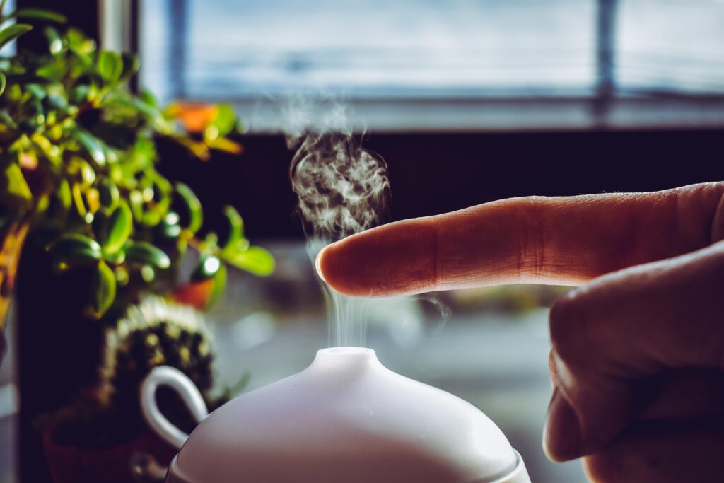 A hand touches mist rising from a diffuser, creating a relaxing ambiance indoors.