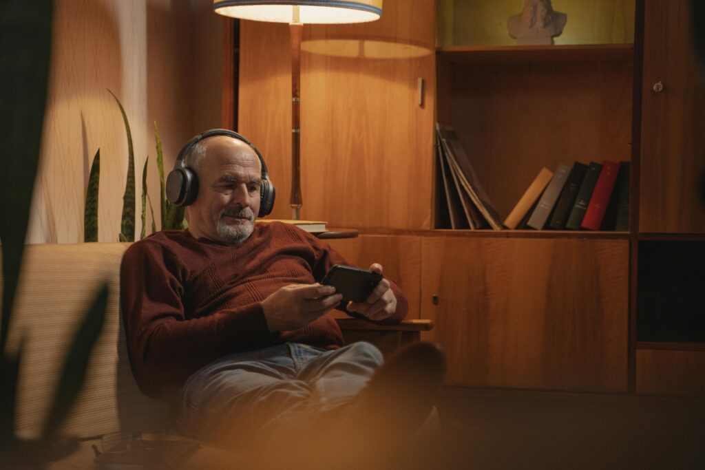 Elderly man enjoying music on headphones while relaxing with a smartphone at home.