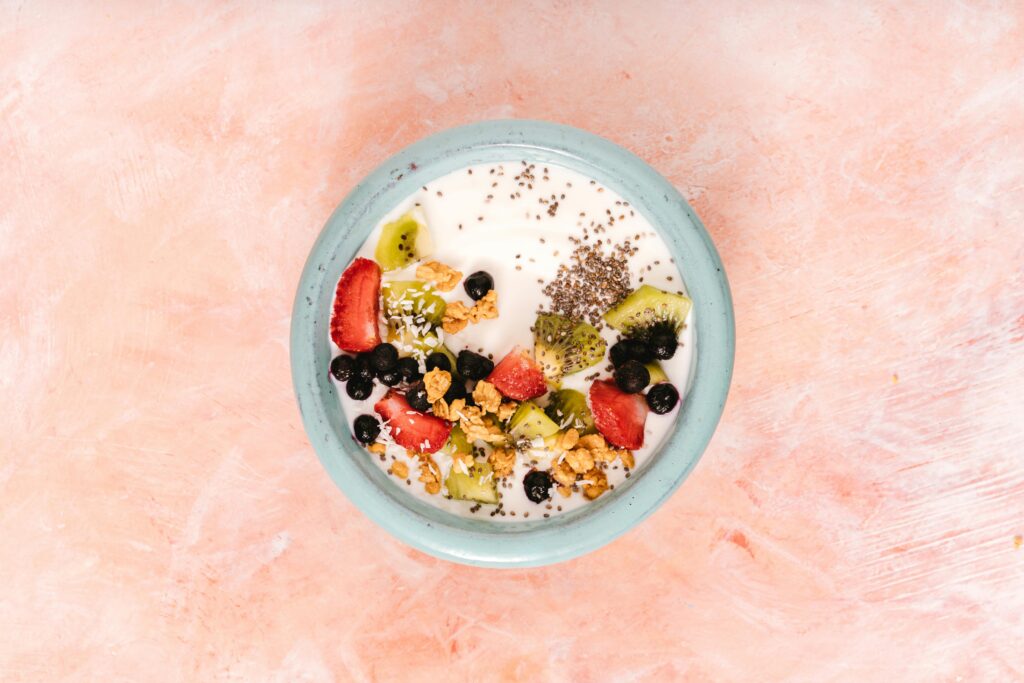 Top view of a nutritious breakfast bowl with yogurt, fresh fruits, and seeds on a pink background.