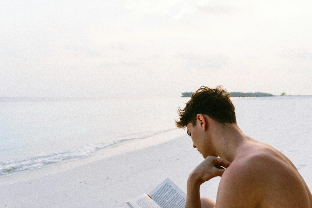 A man enjoys reading a book on a serene Maldives beach, capturing the essence of relaxation.